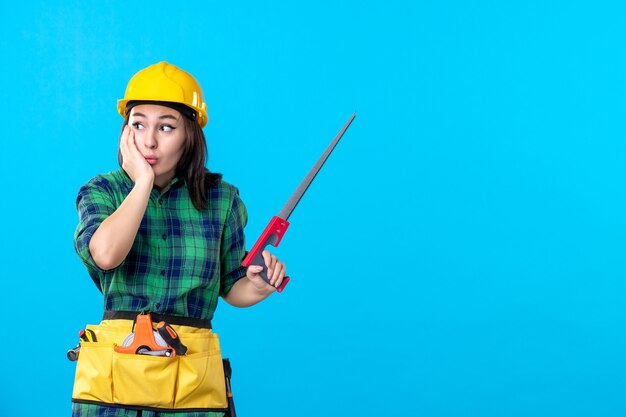 Женщина-строитель, вид спереди, держащая небольшую пилу на синем