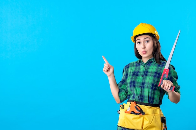 Женщина-строитель, вид спереди, держащая небольшую пилу на синем