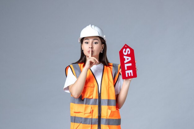 Front view of female builder holding red sale board on gray wall