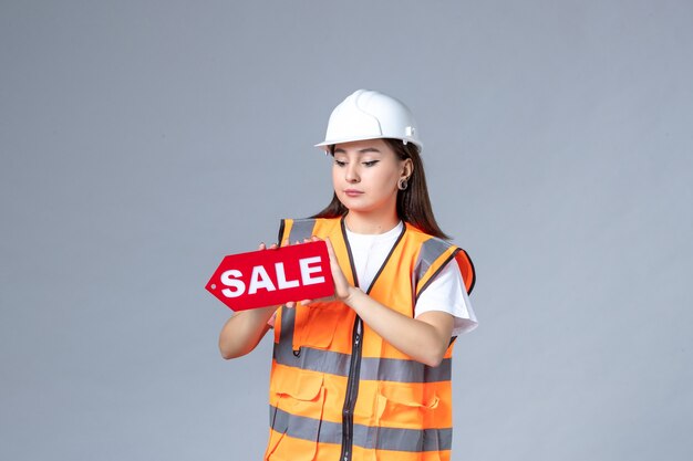 Front view of female builder holding red sale board on white wall