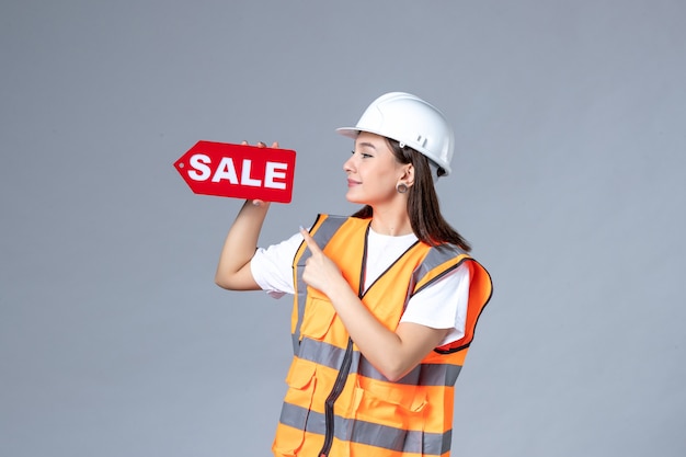 흰 벽에 빨간색 판매 보드를 들고 있는 여성 건축업자의 전면 모습