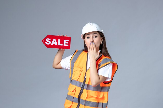 Front view of female builder holding red sale board on white wall