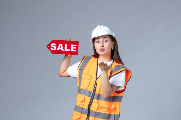 Front view of female builder holding red sale board on white wall