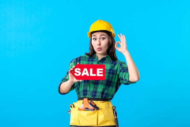 Женщина-строитель, вид спереди, держащая красную распродажу на синем