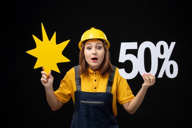 Free photo front view female builder holding yellow figure and on a black wall