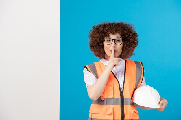 Front view of female builder in uniform on blue wall