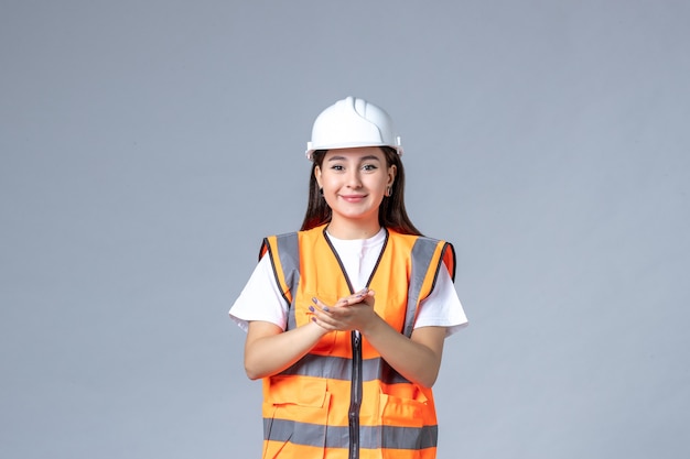 Front view of female builder in uniform clapping on gray wall