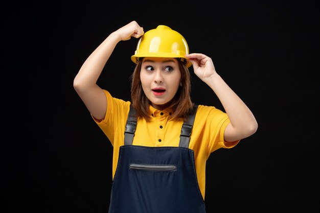 Free photo front view female builder in uniform and helmet on black wall