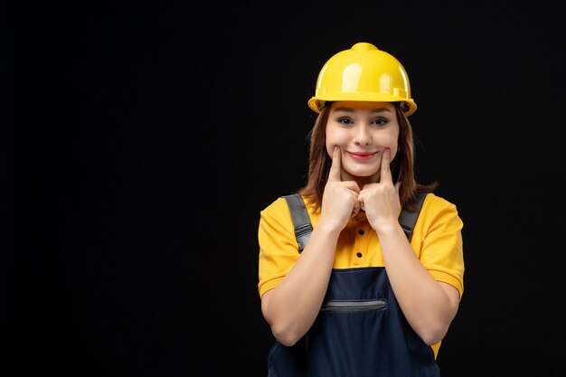 Front view female builder in uniform and helmet on black wall