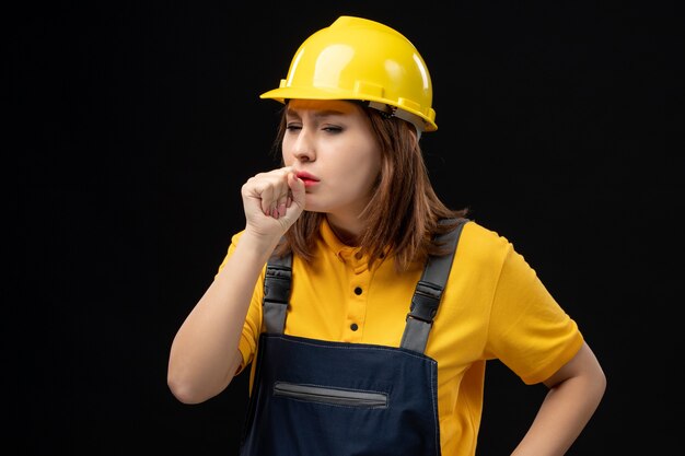 Front view female builder in uniform and helmet on the black wall