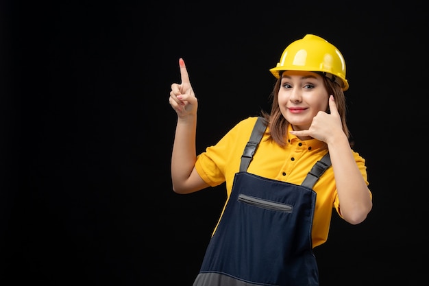 Front view female builder in uniform and helmet on the black wall
