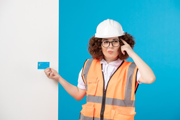 Front view of female builder in uniform and helmet on blue wall