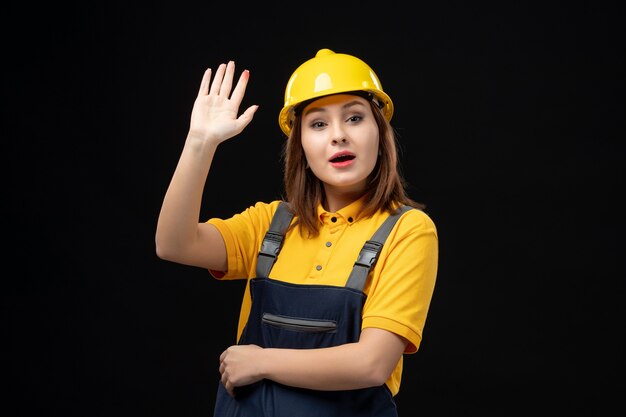 Front view female builder in uniform and helmet waving on black wall