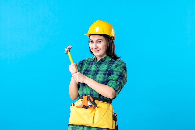 Front view female builder in uniform holding hammer on blue