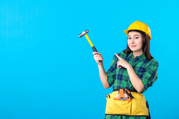 Front view female builder in uniform holding hammer on blue