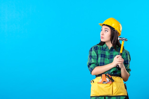 Front view female builder in uniform holding hammer on blue