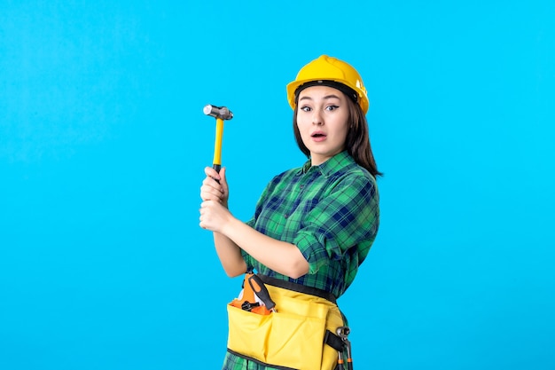 Front view female builder in uniform holding hammer on blue