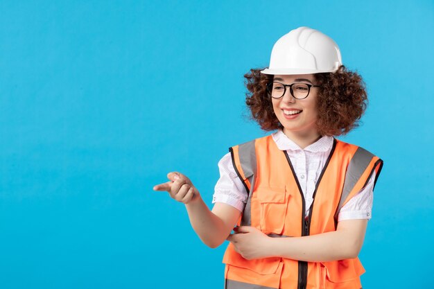 Женщина-строитель в униформе, указывая на что-то на синей стене, вид спереди