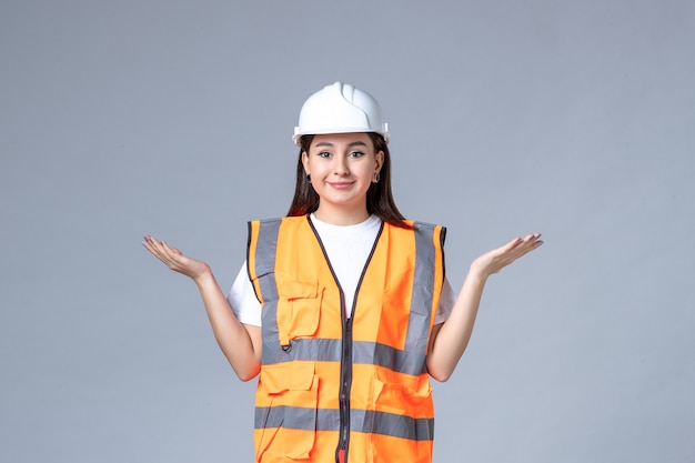 Вид спереди женщины-строителя в униформе и защитном шлеме на серой стене