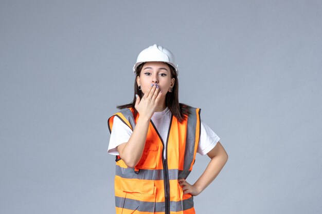 Front view of female builder in uniform and protective helmet on gray wall