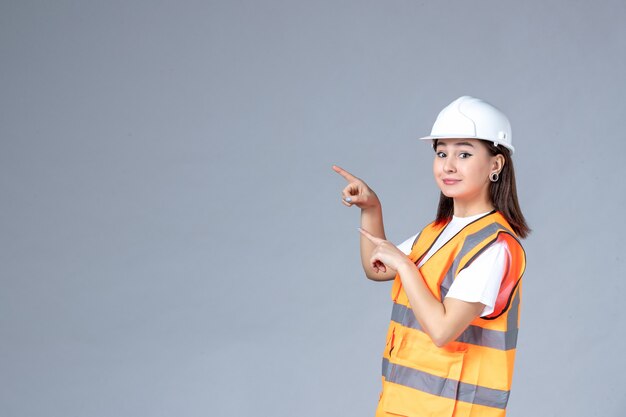 Front view of female builder in uniform smiling on white wall