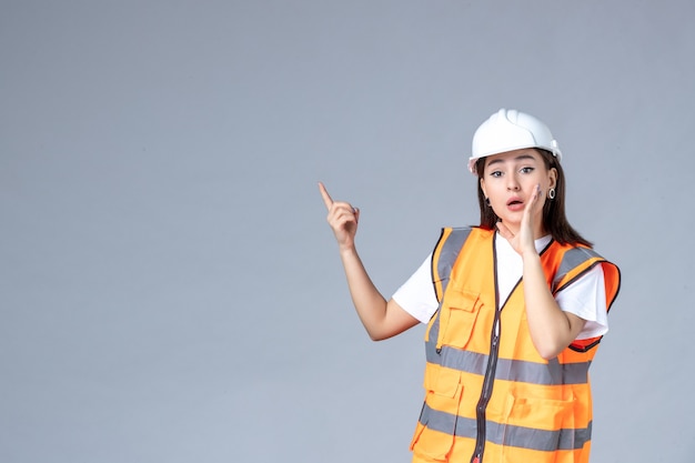 Вид спереди женщины-строителя в униформе, шепчущейся на белой стене