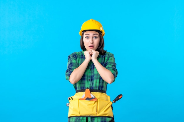 Front view female builder in uniform with different tools on a blue