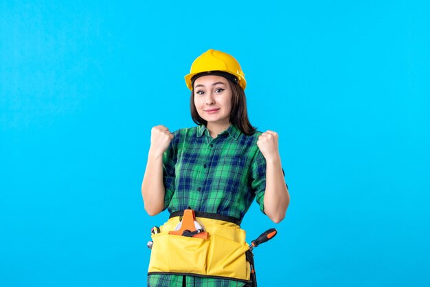 Front view female builder in uniform with different tools on blue