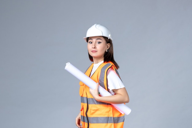 Front view of female builder in uniform with poster in her hands on white wall