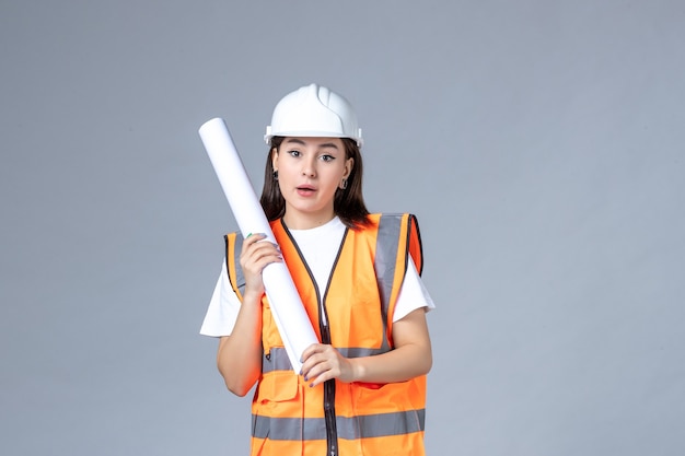 Free photo front view of female builder in uniform with poster in her hands on white wall