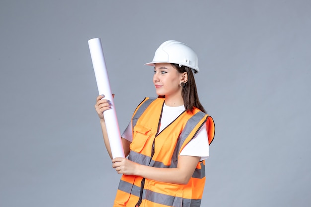 Front view of female builder in uniform with poster in her hands on white wall