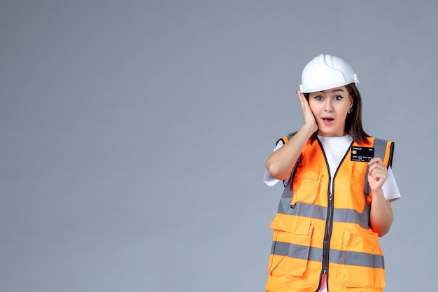Front view of female builder with black bank card in her hands on gray wall