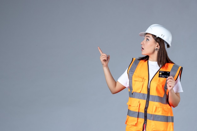 Vista frontale del costruttore femminile con carta di credito nera nelle sue mani sul muro grigio