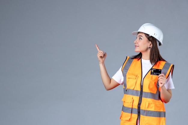 Vista frontale del costruttore femminile con carta di credito nera nelle sue mani sul muro grigio