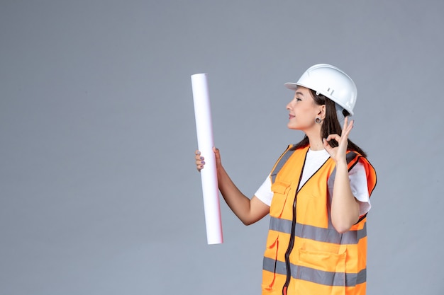 Free photo front view of female builder with poster in her hands on gray wall