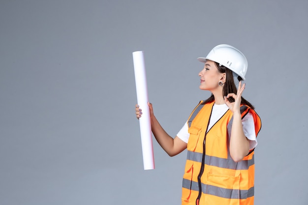 Front view of female builder with poster in her hands on gray wall