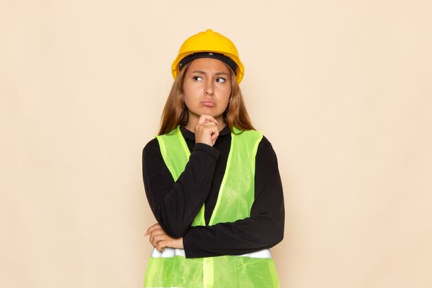 Front view female builder in yellow helmet black shirt posing thinking on the white wall 