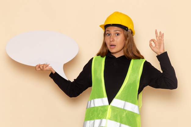 Front view female builder in yellow helmet holding a big white sign on white desk female  architect