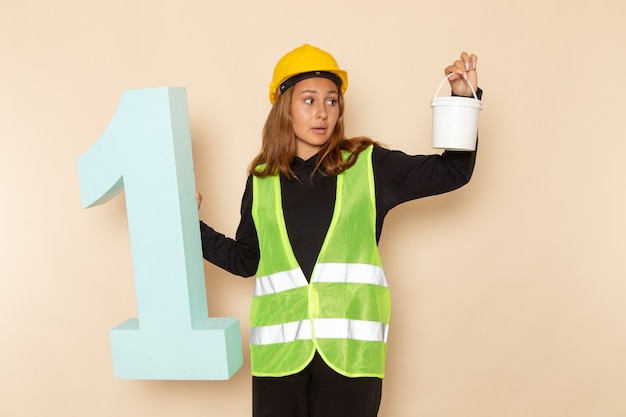 Free photo front view female builder in yellow helmet holding paint and number one figure on the white wall