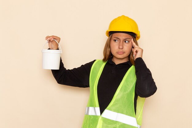 Вид спереди женщина-строитель в желтом шлеме с краской и мышлением на белой стене архитектор-строитель женщина-строитель