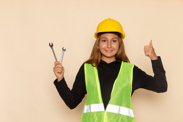 Front view female builder in yellow helmet holding silver instruments on light desk female  architect