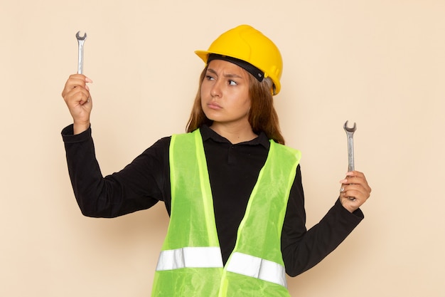 Front view female builder in yellow helmet holding silver instruments on the white wall female builder construction architect