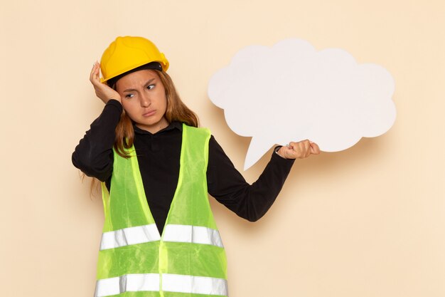 Front view female builder in yellow helmet holding white sign stressfully thinking on white desk female  