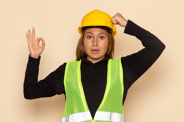 Front view female builder in yellow helmet showing alright sign on the white wall female  