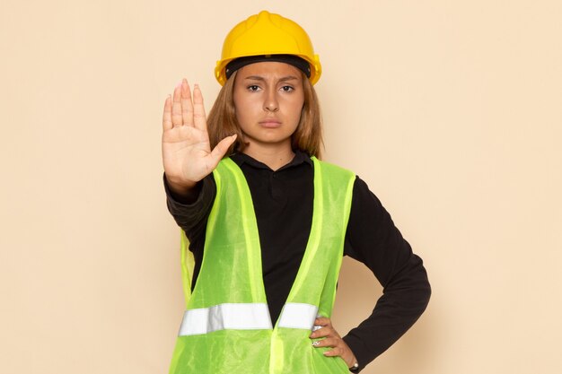 白い壁の女性に一時停止の標識を示す黄色いヘルメットの正面図の女性ビルダー
