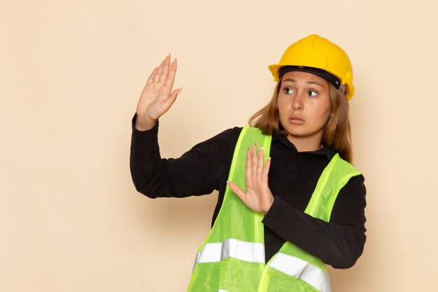 Front view female builder in yellow helmet with cautious expression on the white wall   