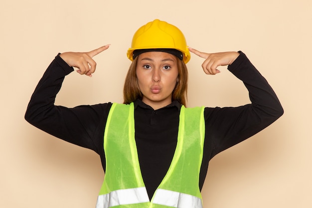 Front view female builder in yellow helmet with cute expression on white wall  