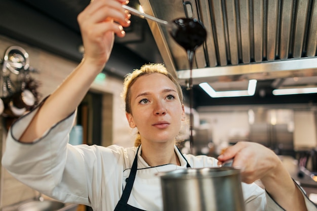 Vista frontale del cuoco unico femminile che controlla lo spessore della salsa