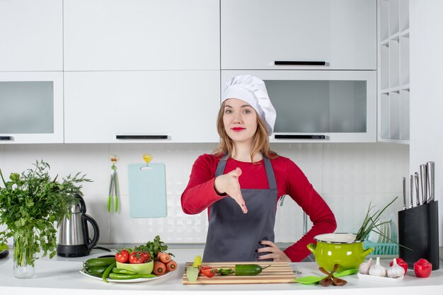 Вид спереди женский шеф-повар в шляпе повара, протягивая руку