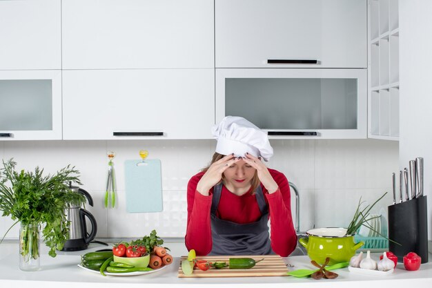 Front view female chef in cook hat holding her head